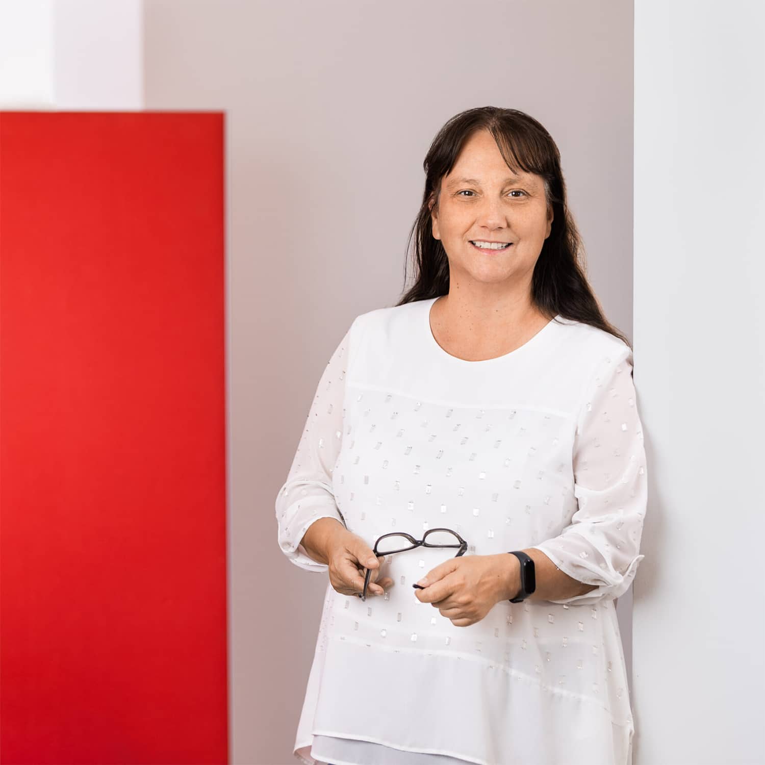 Frau in weißem Oberteil lächelt, hält eine Brille. Schröter GmbH, C-Artikel-Beschaffung und E-Procurement in der Bürowirtschaft.