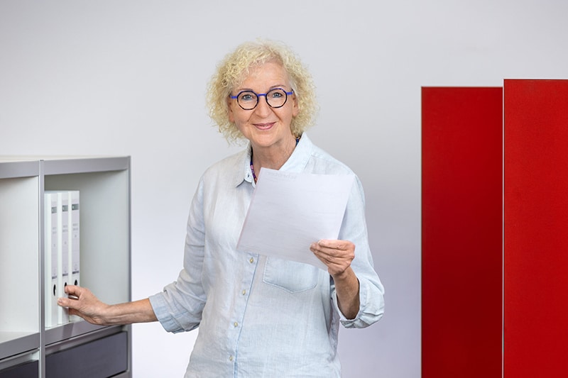 Mitarbeiterin im Büro lächelnd mit Dokument. Schröter GmbH optimiert C-Artikel-Beschaffung für effiziente Geschäftsabläufe.