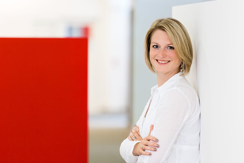 Mitarbeiterin in weißem Hemd lächelt in moderner Büroeinrichtung. Schröter GmbH optimiert C-Artikel-Beschaffung.