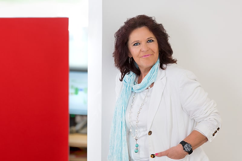 Mitarbeiterin lehnt an roter Wand, repräsentiert Schröter GmbH, Anbieter für C-Artikel-Beschaffung.