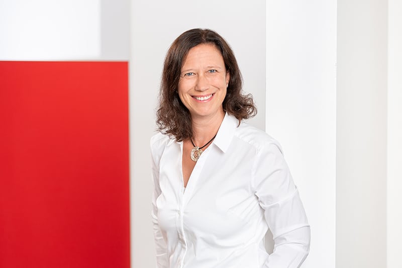 Mitarbeiterin lächelt vor rotem Hintergrund, Schröter GmbH, C-Artikel-Beschaffung und E-Procurement-Lösungen.