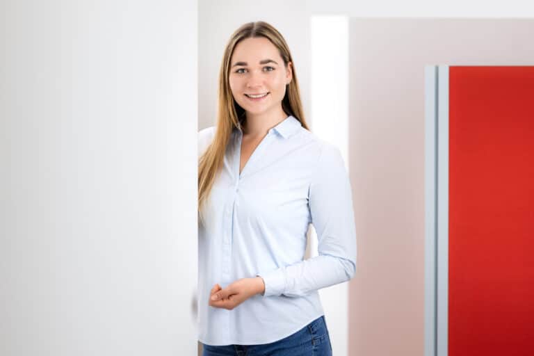 Junge Frau in Büroumgebung, lächelnd, repräsentiert Schröter GmbH, Spezialist für C-Artikel-Beschaffung und E-Procurement.