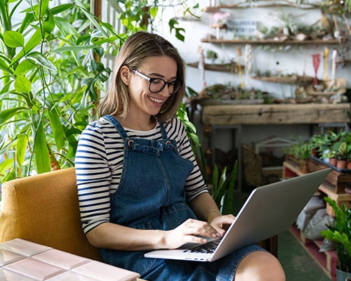 Frau arbeitet fröhlich am Laptop in einem grünen Büro, symbolisiert effizientes C-Artikel-Management bei Schröter GmbH.