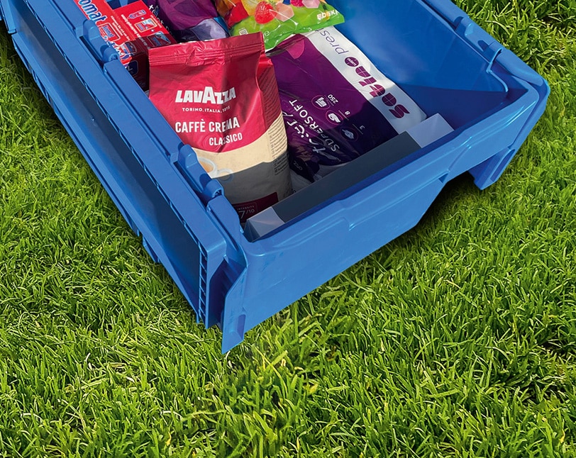 Blaue Kiste mit verschiedenen Produkten auf einer grünen Wiese, Symbol für effiziente C-Artikel-Beschaffung durch Schröter GmbH.